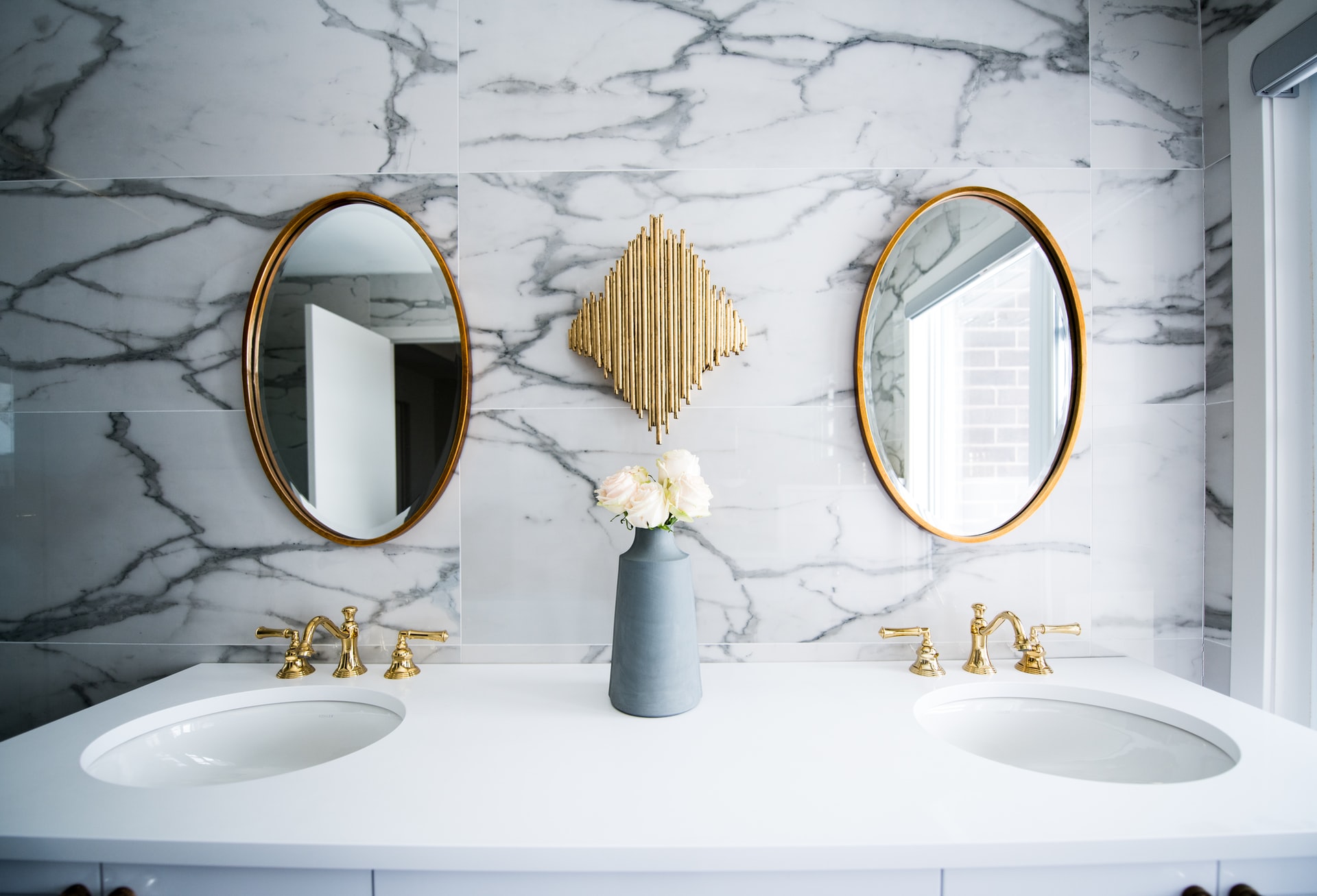 Two Gold Oval Mirrors Hanging On Marble Bathroom Wall above Bathroom Sinks